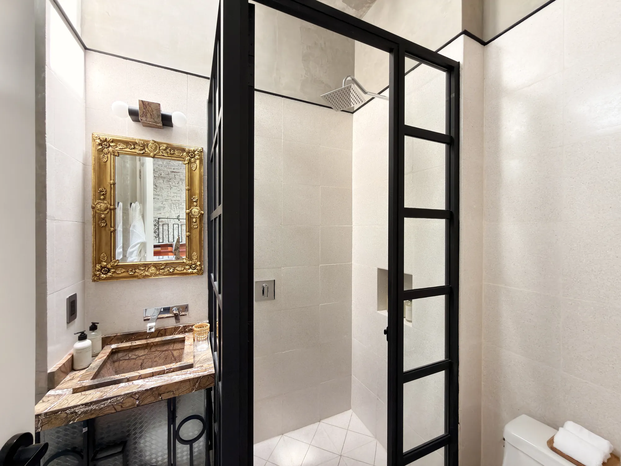 The bathroom: a marble sink with a gold mirror and a shower with a glass door and black ironwork