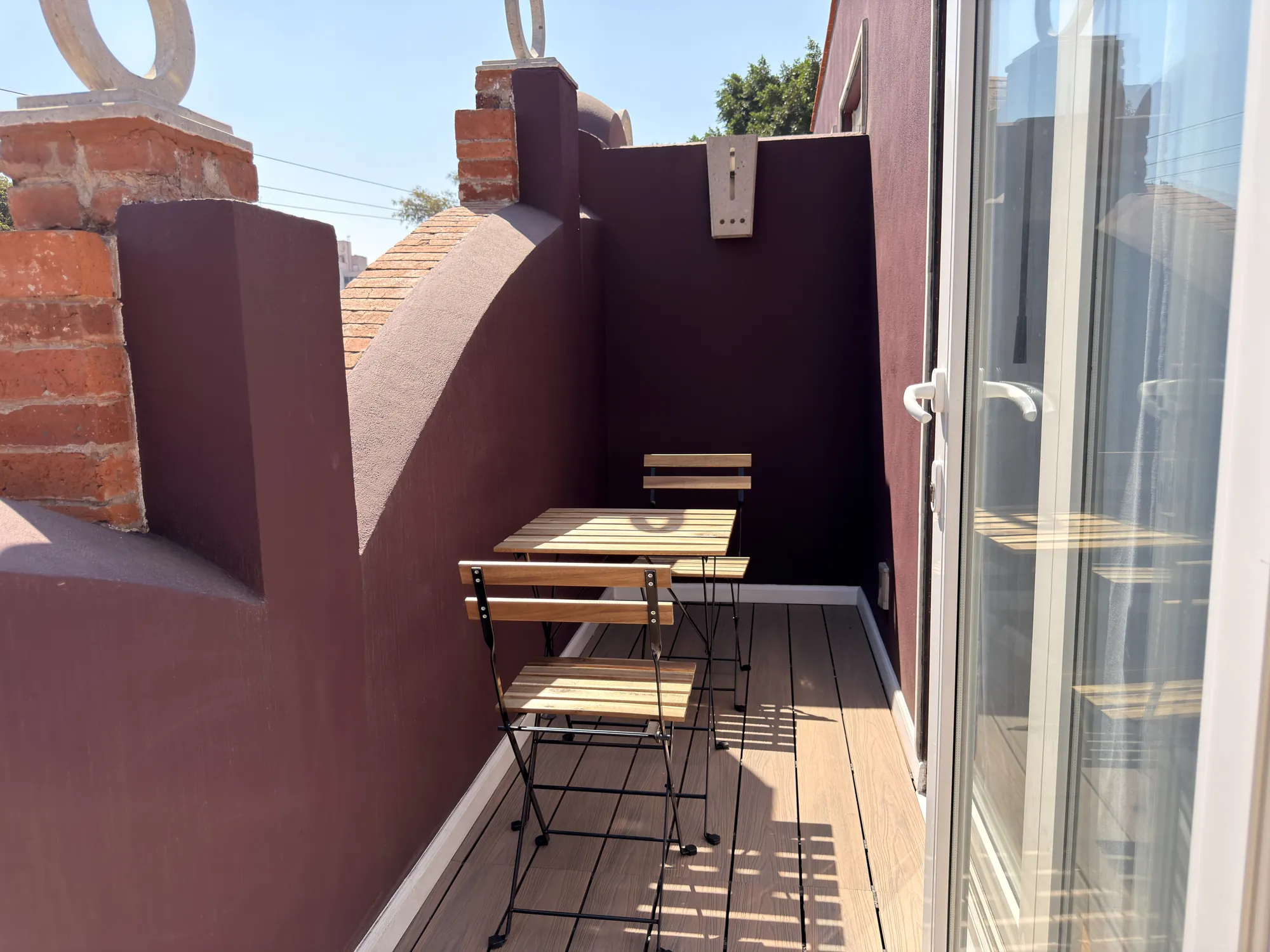 The private balcony with a table and two folding wooden chairs, beside the glass door