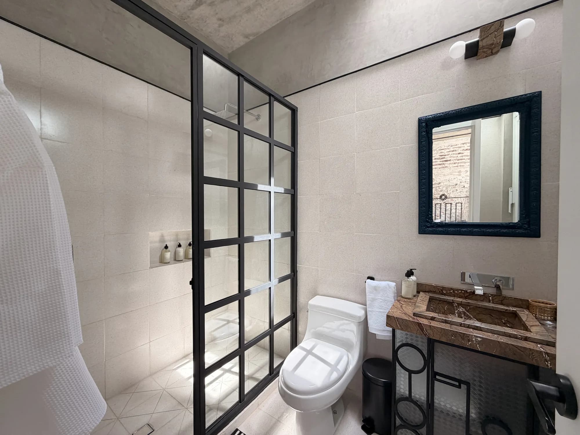 The bathroom with a glass shower and black ironwork, a marble sink and a blue mirror