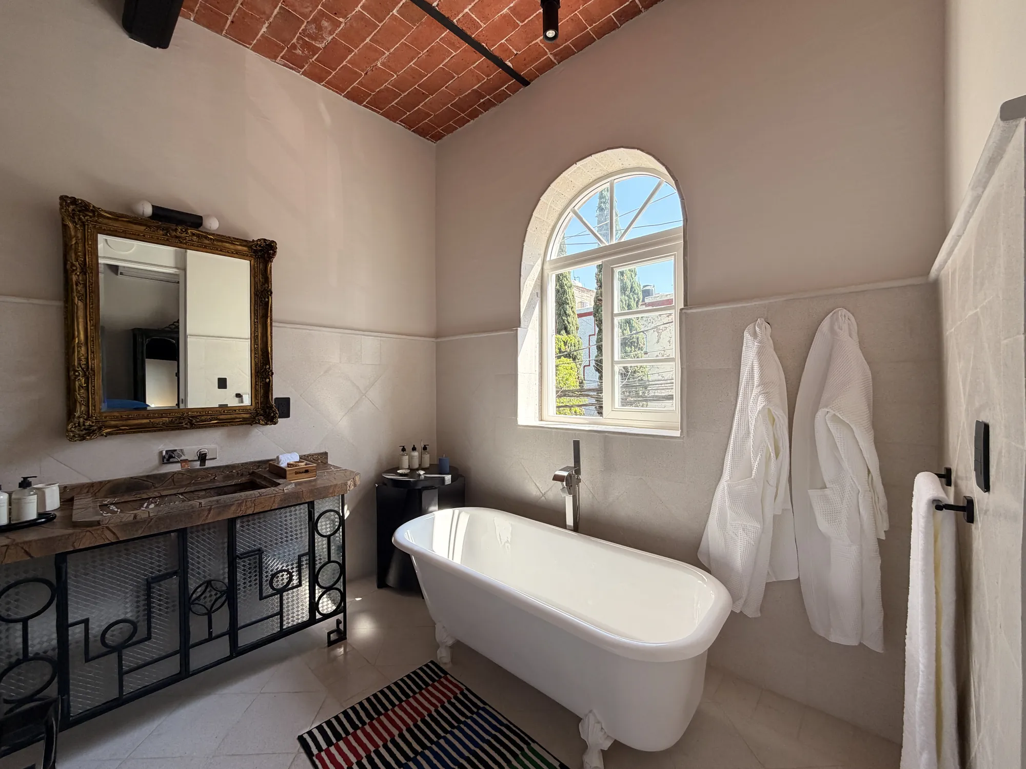 The bathroom with a clawfoot tub, an arched window and hanging robes
