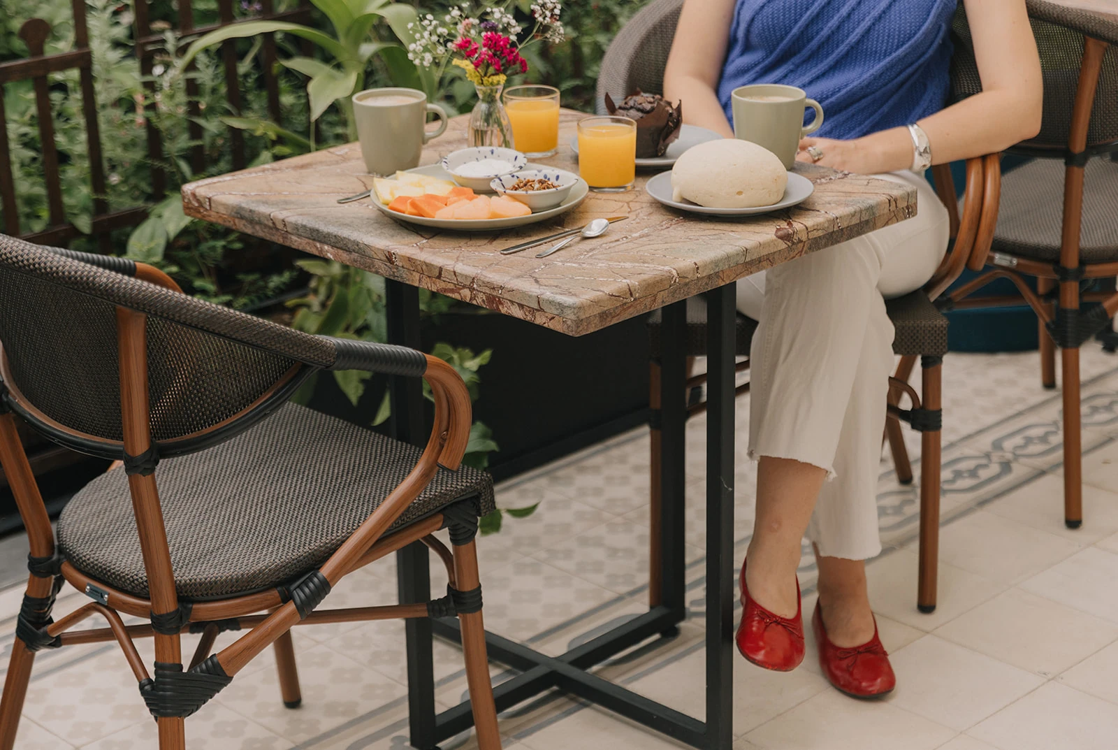 The breakfast table on the garden terrace, with a guest in a blue blouse and red shoes among the rattan chairs