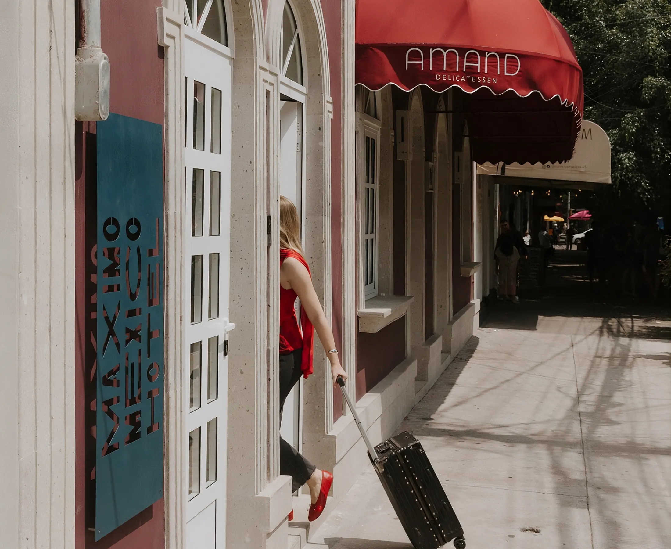 The red awning of Amand Delicatessen on the ground floor of the building, beside the hotel door, with its terrace tables behind