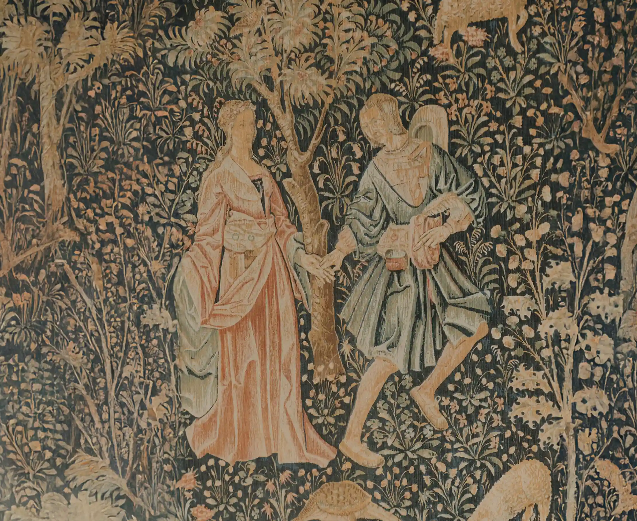 An antique tapestry with two figures among foliage and flowers