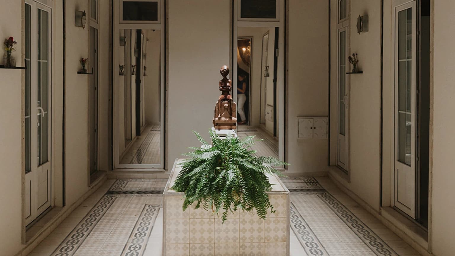 A symmetrical corridor with mirrored doors, tiled floor and a fern as its centrepiece