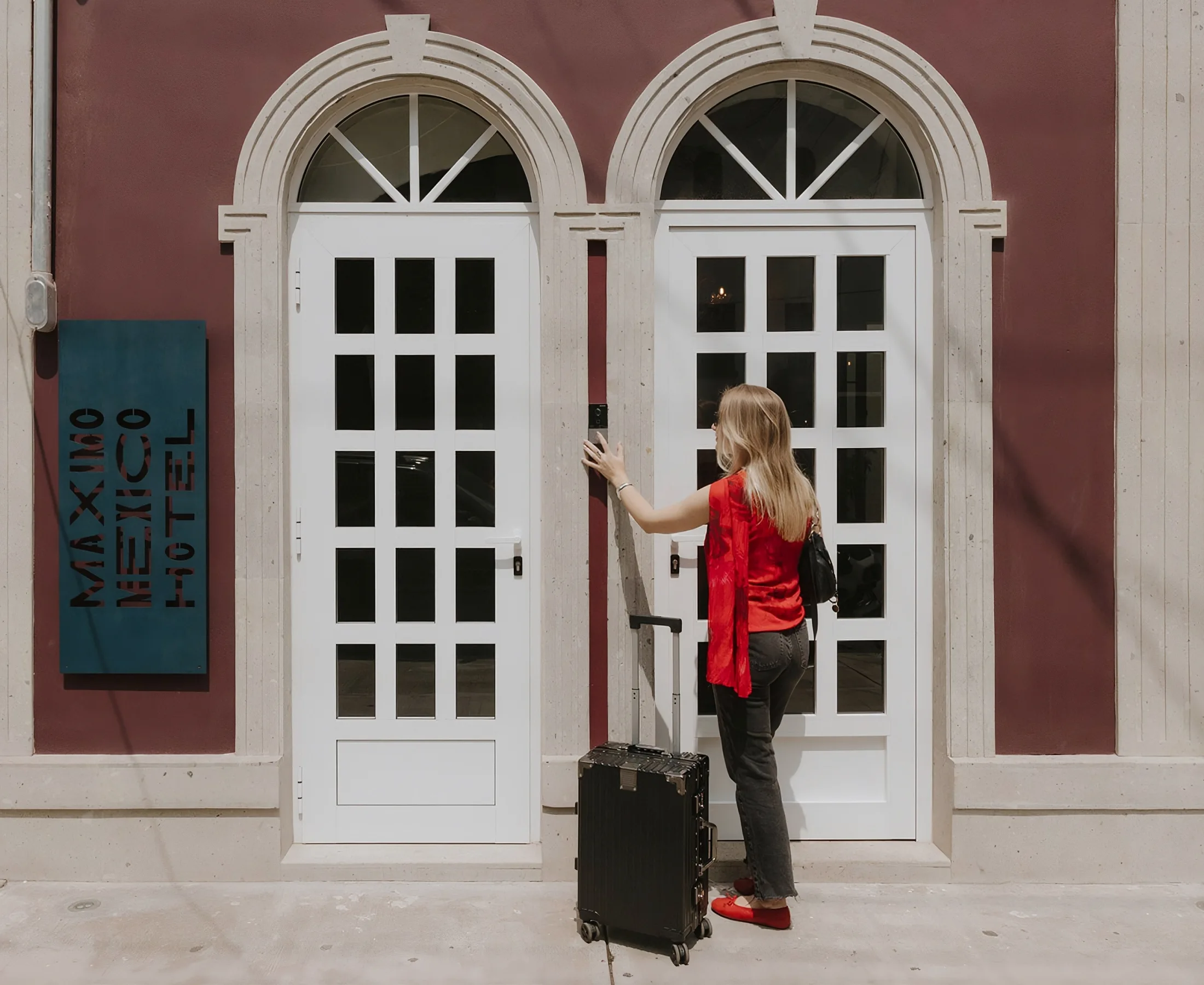 A guest with a suitcase rings the bell at the facade, beside the "Máximo México Hotel" sign