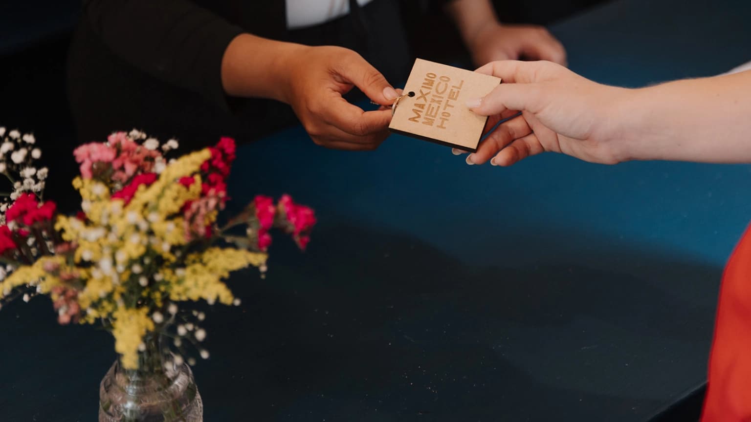 The wooden key tag with the hotel's name, handed over at the front desk beside a flower arrangement