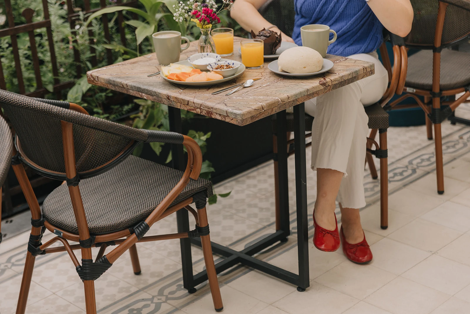 The terrace table with breakfast served and the legs of a guest in red shoes, among the rattan chairs