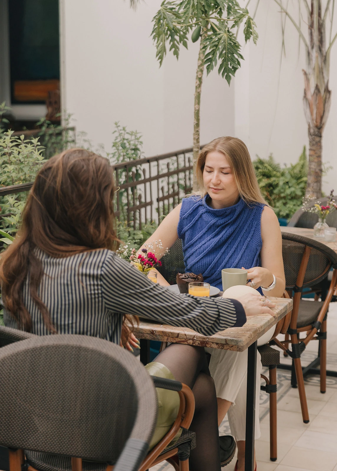 A guest in a blue blouse drinking orange juice on the garden terrace, seated at a marble table among plants
