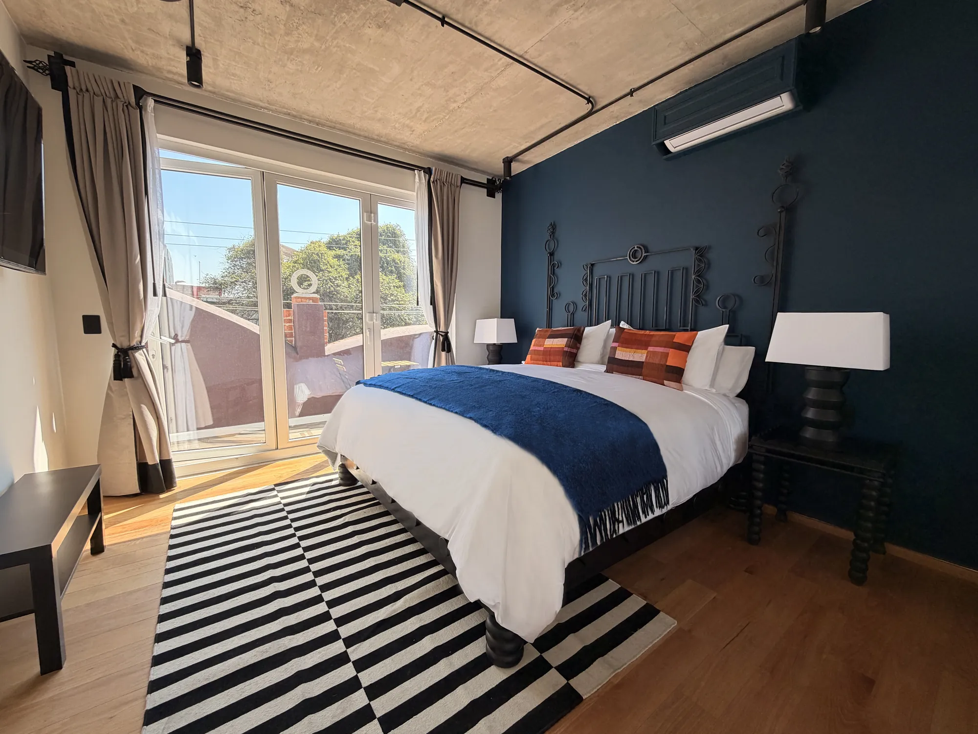 The King bed beside the balcony door, with curtains and a striped rug