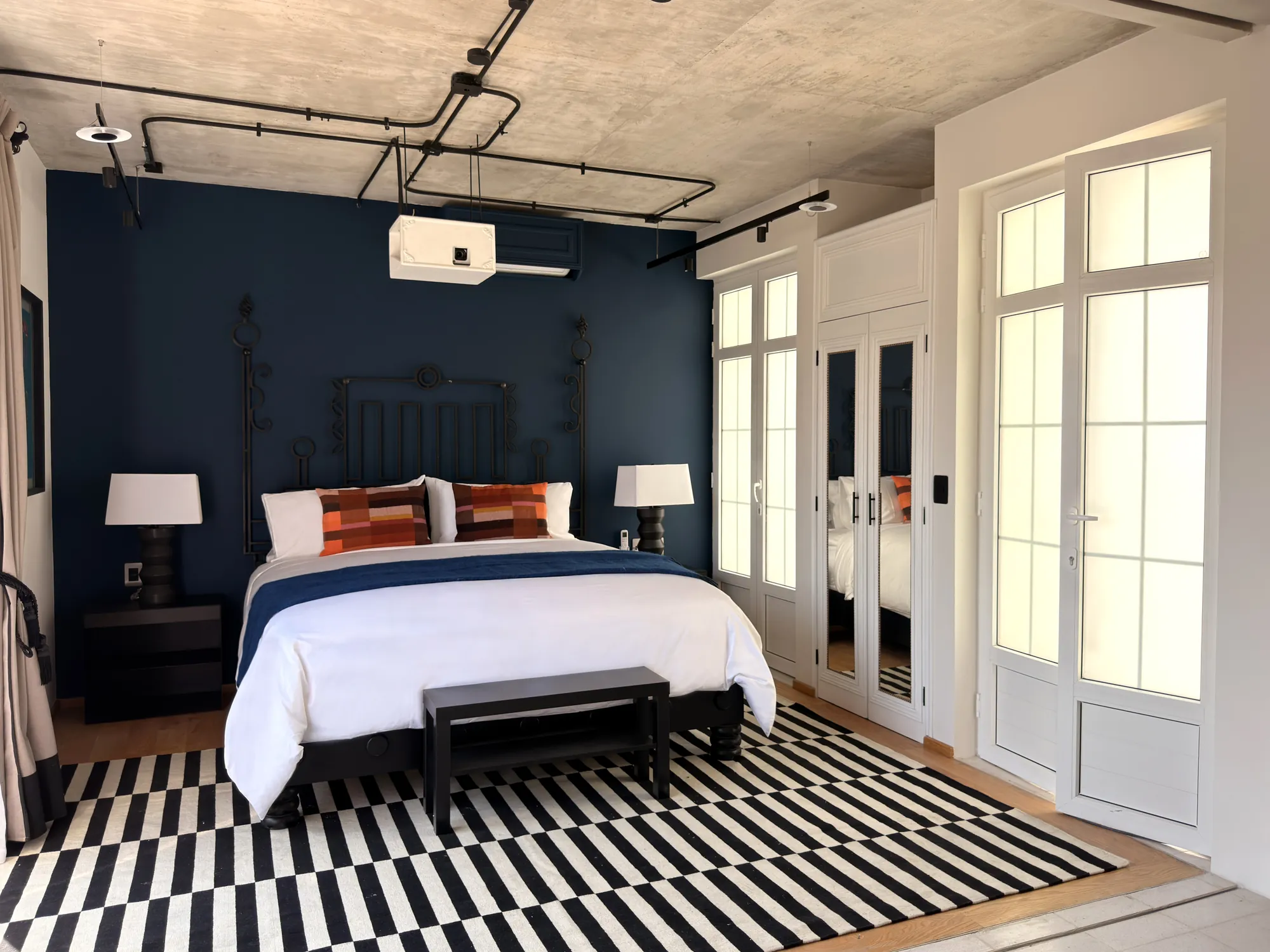 The bed facing the blue wall, with the projector on the ceiling and the French doors