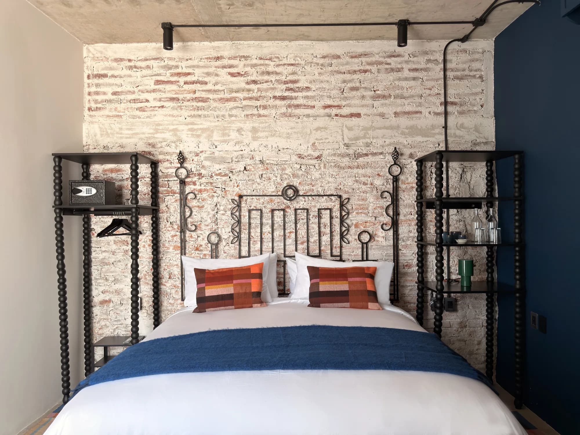 The King bed seen head-on, between two black shelves of turned wood, under the brick wall