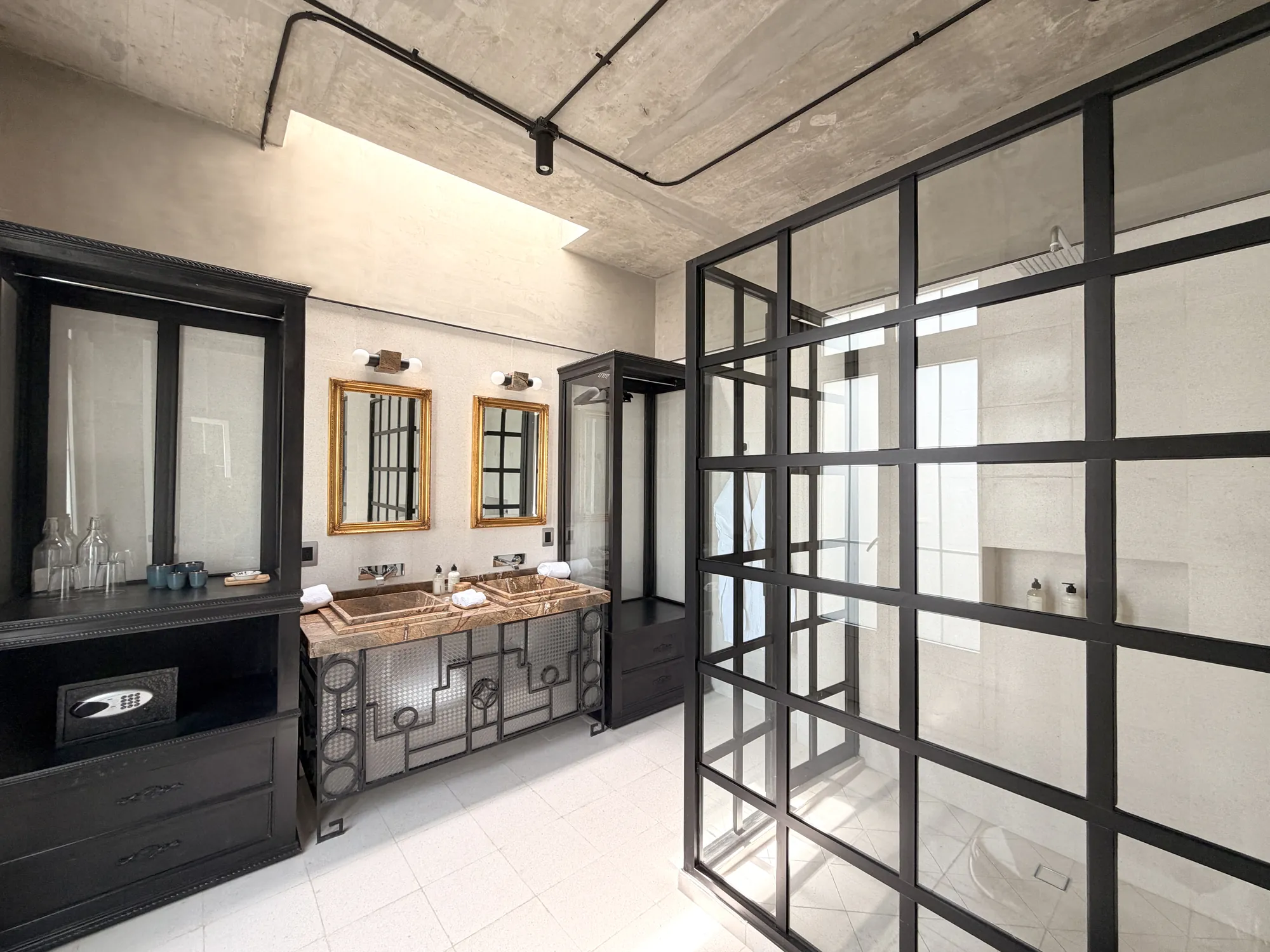 The bathroom with the dressing area and the shower behind glass with black ironwork