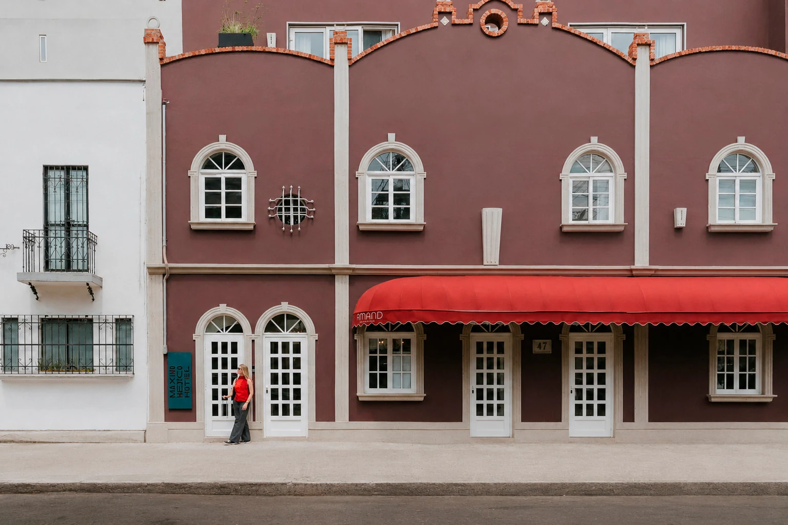 The wine-coloured facade of the house with its red awning, seen from Manzanillo street, with a guest in front of the door